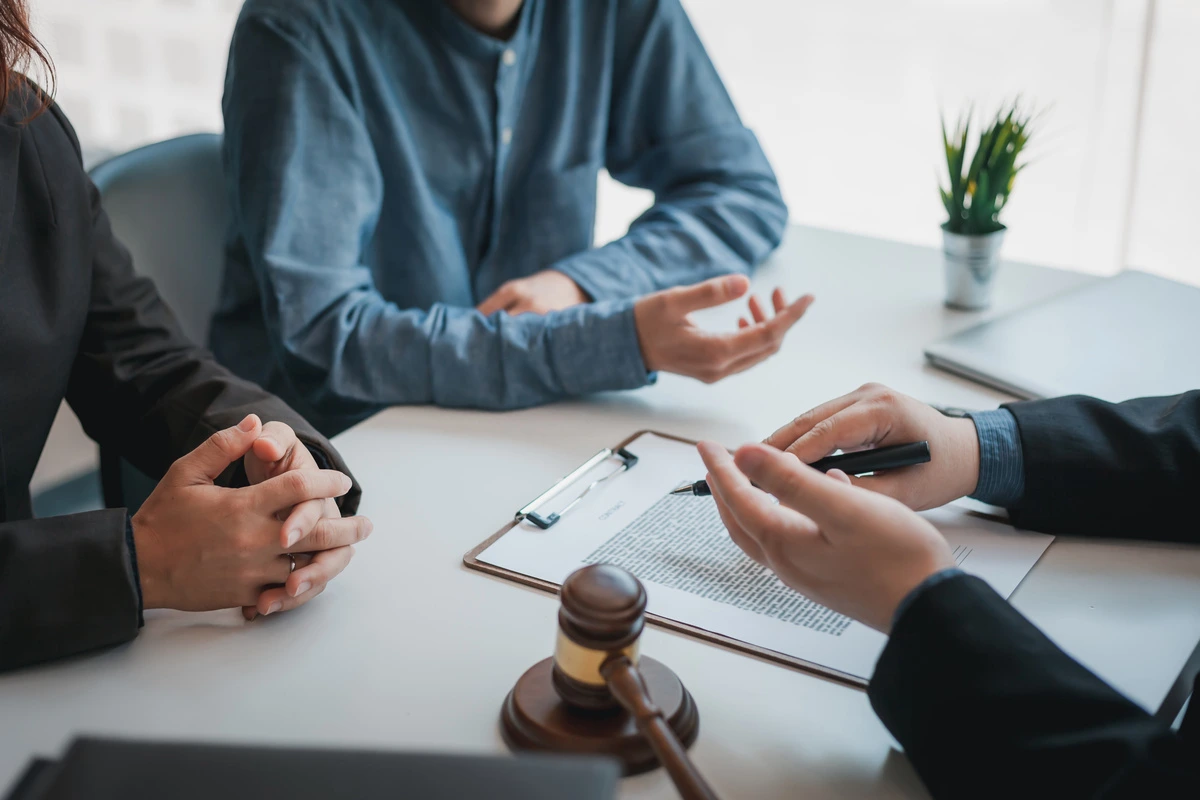 Un avocat consultant deux clients avec des documents juridiques et un marteau de juge sur la table, représentant une réunion de conseil juridique pour la résolution d'un litige ou d'un contrat.