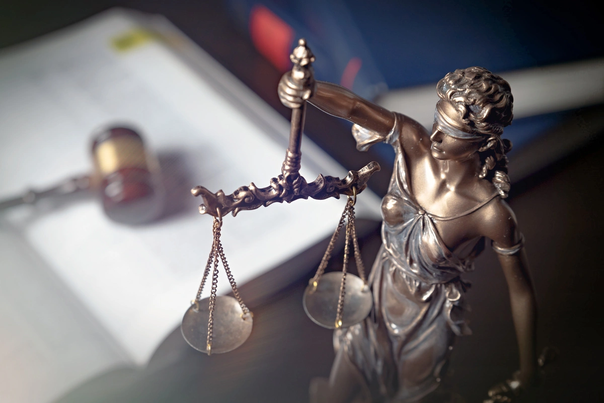 Une statue de la justice avec un marteau de juge en arrière-plan, illustrant les principes de justice et de droit public dans un contexte juridique.