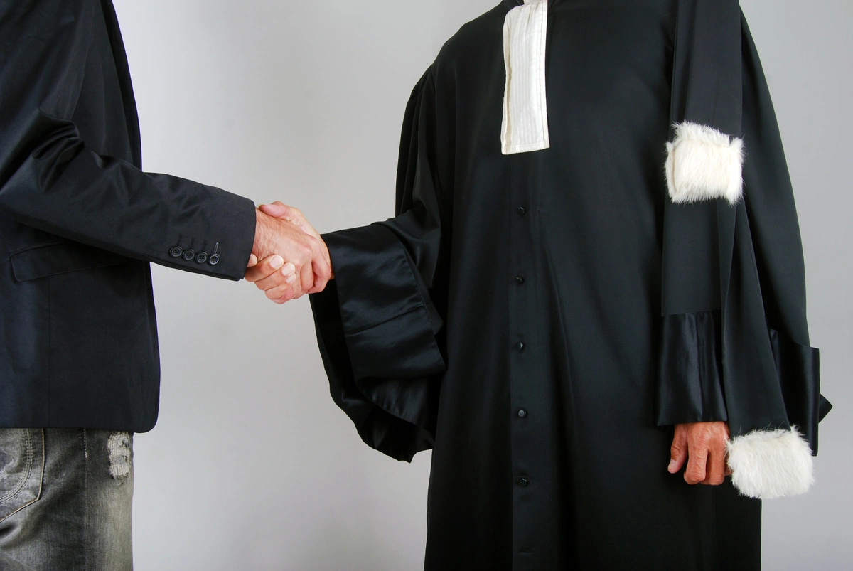 Poignée de main entre un avocat en robe et son client, marquant l'accord de collaboration pour une affaire de droit de l'urbanisme.